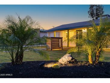 Charming home exterior featuring a manicured lawn, palm trees, and illuminated landscaping rocks at 1818 W Highland Ave, Phoenix, AZ 85015