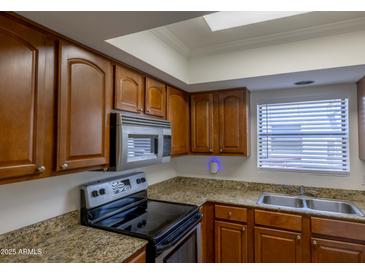 Well-lit kitchen features granite countertops, stainless steel appliances, and wood cabinets at 3330 W Danbury Dr # E203, Phoenix, AZ 85053