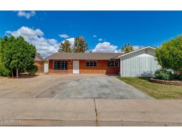 Charming brick home features a spacious driveway, mature trees, and lush landscaping at 3126 W Stella Ln, Phoenix, AZ 85017