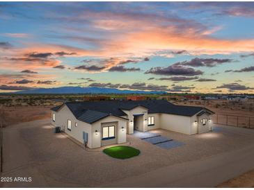 Stunning single-story home featuring a neutral palette, dark roof, and desert landscaping at twilight at 28848 W Grand Ave, Wittmann, AZ 85361