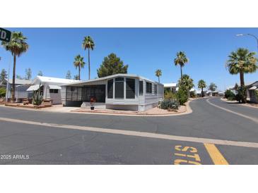 Well-maintained mobile home featuring desert landscaping and a screened-in porch, situated on a corner lot with palm trees at 111 S Greenfield -- # 602, Mesa, AZ 85206