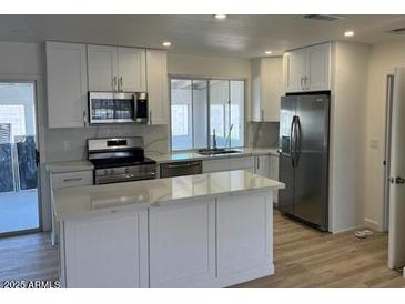 Bright kitchen features white cabinets, stainless appliances, and island with marble countertop at 18045 N 20Th N Ln, Phoenix, AZ 85023