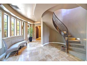 Bright foyer featuring travertine floors, a curved staircase with iron railing, and a comfortable sitting area at 3804 E Camelback Rd, Phoenix, AZ 85018