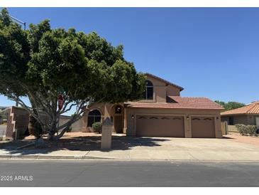 Inviting two-story home with a three-car garage, lush tree, and warm, earthy tones at 2213 N Ashbrook Cir, Mesa, AZ 85213