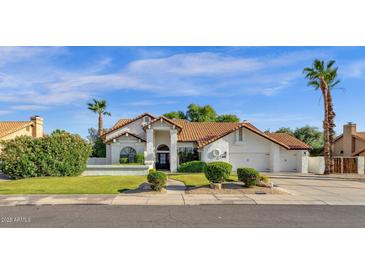 Beautiful single-story home with a tile roof, manicured lawn, mature trees, and a three-car garage at 9821 E Windrose Dr, Scottsdale, AZ 85260