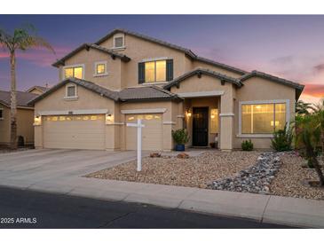 Inviting two-story home featuring a three-car garage, neutral stucco and desert landscaping at dusk at 18030 W Caribbean Ln, Surprise, AZ 85388