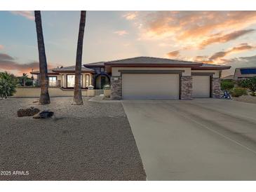 Charming home featuring a three-car garage, stone accents, and a meticulously landscaped front yard under a colorful sky at 15532 W Prairie Dunes Dr, Surprise, AZ 85374