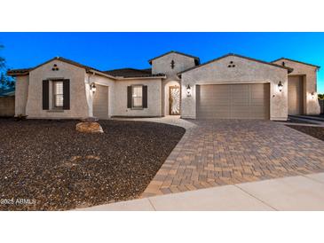 Home exterior showcasing a three-car garage, gravel landscaping, and a brick paver driveway at 18371 W Roma Ave, Goodyear, AZ 85395