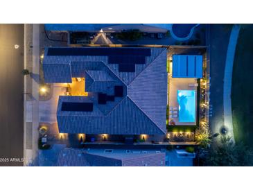 Aerial view of a home with a pool and an outdoor kitchen area illuminated by landscape lighting at dusk at 17018 W Saguaro Park Ln, Surprise, AZ 85387