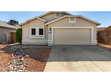 Beige single-story home featuring a two car garage and desert landscaping in front at 8668 N 107Th Dr, Peoria, AZ 85345