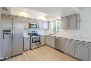 Updated kitchen features stainless steel appliances, gray cabinets, light countertops and wood-look flooring at 3811 S Mill Ave, Tempe, AZ 85282