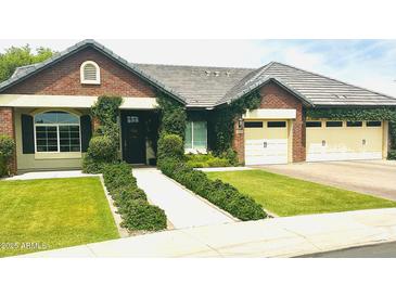 Charming brick home with a well-manicured lawn, lush greenery, and a three-car garage at 4824 S Brice --, Mesa, AZ 85212