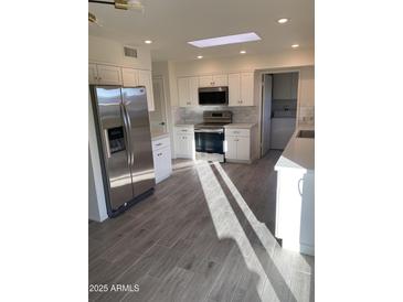 Bright kitchen featuring stainless steel appliances, white cabinets, tiled backsplash, and wood-look tile flooring at 10025 W Shasta W Dr, Sun City, AZ 85351