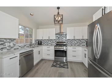 Modern kitchen boasts stainless steel appliances, granite countertops, stylish mosaic backsplash, and ample white cabinetry at 11224 W Puget Ave, Peoria, AZ 85345