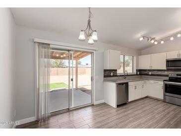 Bright kitchen with white cabinets, stainless steel appliances, and wood-look flooring with sliding door access to back yard at 19802 N 3Rd Ave, Phoenix, AZ 85027