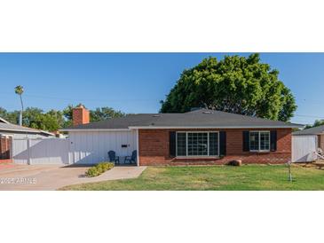 Charming brick home with a well-maintained lawn, a black roof, a brick chimney and a cozy front entrance with chairs at 1909 E Bethany Home Rd, Phoenix, AZ 85016