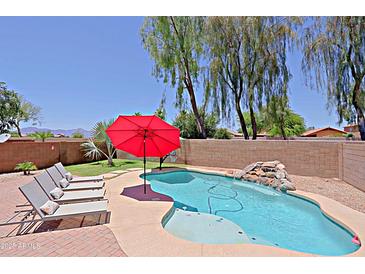 Beautiful backyard pool with waterfall feature, red umbrella, and lounge chairs perfect for relaxing at 42812 W Venture Rd, Maricopa, AZ 85138