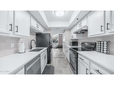 Galley kitchen with white cabinets, quartz countertops, black appliances and subway tile backsplash at 2615 N Hayden Rd # 114, Scottsdale, AZ 85257