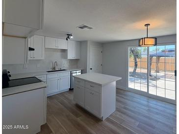 A bright kitchen features a kitchen island, wood flooring, white cabinets and stainless steel appliances at 5951 W Granada Rd, Phoenix, AZ 85035