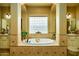 Elegant bathtub with tile surround, decorative window, and arched entranceways leading to dual vanities at 12797 S 179Th Dr, Goodyear, AZ 85338