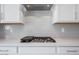 Close-up of a kitchen with white cabinets and a grey backsplash behind the stove at 8746 W Denton Ln, Glendale, AZ 85305