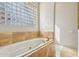 Relaxing bathroom featuring a soaking tub with gold fixtures, marble surround, and glass block window at 9853 E Sundance Trl, Scottsdale, AZ 85262