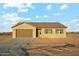 A single-story tan home with a brown roof, brown shutters, and a two-car garage under a cloudy blue sky at 31824 N 221St Dr, Wittmann, AZ 85361