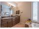 Bathroom with dual sinks, granite countertops, wood cabinets, and a large window with plantation shutters at 37269 N 100Th Pl, Scottsdale, AZ 85262