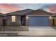 Single story home at dusk with a large driveway, desert landscaping, and a gray accent door at 16025 W Cottontail Ln, Surprise, AZ 85387