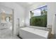 Bright bathroom with a soaking tub beneath a large window overlooking a lush, private garden at 8675 E Thoroughbred Trl, Scottsdale, AZ 85258