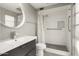 Modern bathroom featuring a stylish vanity, large round mirror, and walk-in shower with white tiling and a glass door at 11133 W Cameo Dr, Sun City, AZ 85351