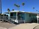 Cute aqua-colored manufactured home with covered porch, ramp, and mature palm trees at 9501 E Broadway Rd # 165, Mesa, AZ 85208