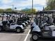 Row of golf carts lined up and ready for use, surrounded by trees, blue sky and other parked cars at 25609 N Forest Rd # 13, Rio Verde, AZ 85263