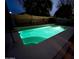 Backyard in-ground pool with illuminated water, surrounded by patio and block wall, perfect for nighttime relaxation at 12742 W Ash St, El Mirage, AZ 85335
