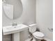 Powder room featuring a pedestal sink, round mirror, toilet, and modern fixtures at 8975 S 168Th Ln, Goodyear, AZ 85338