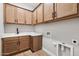 Functional laundry room with wooden cabinets, sink, and tile floors for easy cleaning and ample storage at 32962 N 131St Dr, Peoria, AZ 85383
