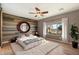 A cozy bedroom with a wood accent wall, a ceiling fan, light hardwood floors, and a large window that lets in natural light at 29007 N 120Th Dr, Peoria, AZ 85383