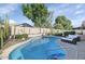 An in-ground pool with a sunning area and patio seating, surrounded by mature landscaping and tall cacti at 3244 E Hononegh Dr, Phoenix, AZ 85050