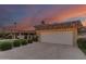 Attached two-car garage featuring white doors, lighting, a tile roof, and landscaping against a colorful dusk sky at 9734 N 105Th Dr, Sun City, AZ 85351