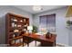 Well-lit home office featuring a wooden desk, built-in bookshelves, and a window with blinds at 5322 W Coles Rd, Laveen, AZ 85339