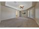 Spacious carpeted main bedroom featuring a tray ceiling, ceiling fan, and access to the bathroom at 18009 W Denton Ave, Litchfield Park, AZ 85340