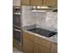 Modern kitchen features a smooth cooktop, stainless double oven, granite counters, and decorative tile backsplash at 10731 W Mission Ln, Sun City, AZ 85351