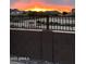 A back yard view through a black iron fence and cinder block wall with the setting sun beyond at 32040 N Lisadre Ln, San Tan Valley, AZ 85144