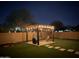 Nighttime view of a backyard with a lighted pergola, swing, and a neatly landscaped lawn at 55 N Abalone Ct, Gilbert, AZ 85233