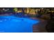 Blue illuminated pool at night with rock waterfall feature at 45707 W Barbara Ln, Maricopa, AZ 85139