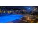 Blue illuminated pool at night with rock waterfall and patio furniture at 45707 W Barbara Ln, Maricopa, AZ 85139