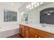 Bright bathroom showcasing dual sinks, wood cabinets, and a window above the soaking tub at 14995 W Desert Hills Dr, Surprise, AZ 85379