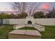 Outdoor fireplace on a green lawn surrounded by concrete bench seating against a wall and silhouetted trees at 3457 E Ellis St, Mesa, AZ 85213