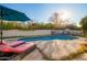 Sun-drenched backyard pool with lounge chairs, umbrella, and a view of the outdoor fireplace at 3457 E Ellis St, Mesa, AZ 85213