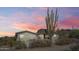 Charming single-story home with desert landscaping, a black roof and wrought iron fence under a colorful sunset sky at 5428 E El Sendero Dr, Cave Creek, AZ 85331